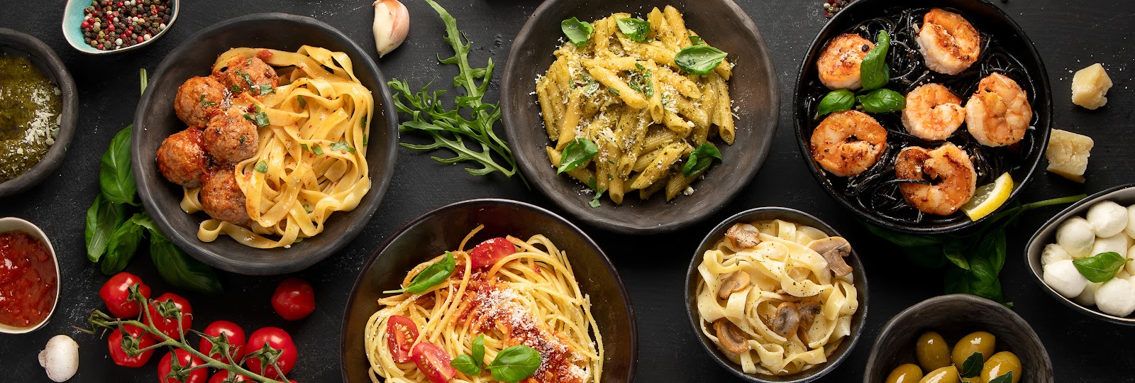 Overhead spread of Italian pasta dishes on a dark table