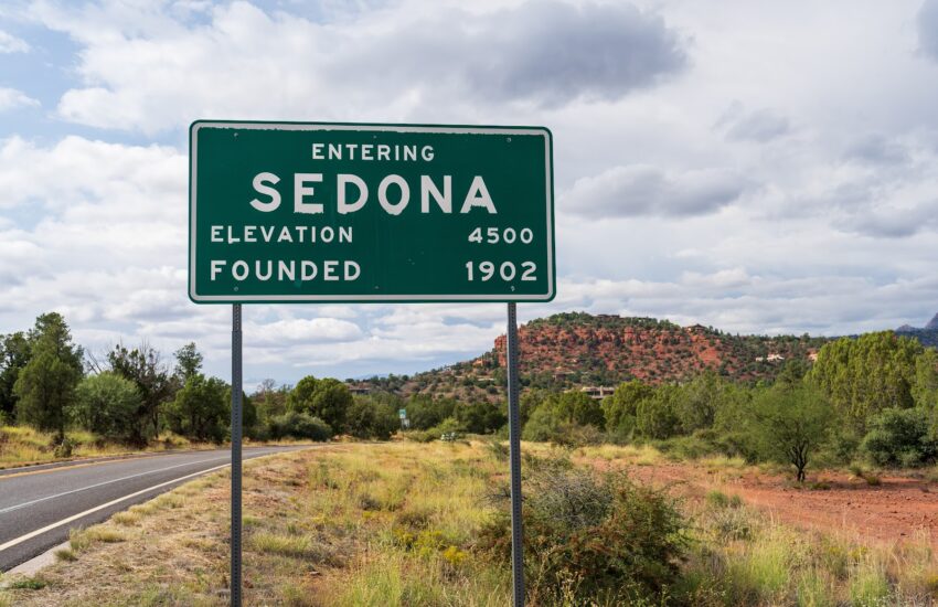 Entering Sedona road sign with red rock formations behind it