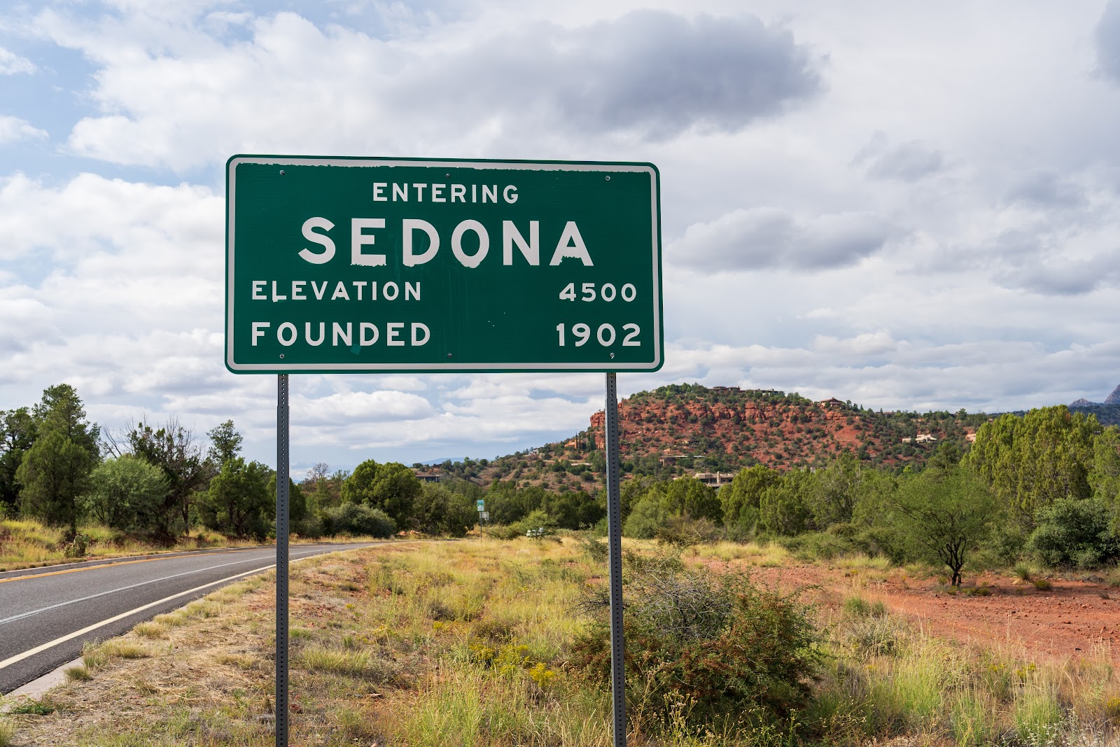 Entering Sedona road sign with red rock formations behind it