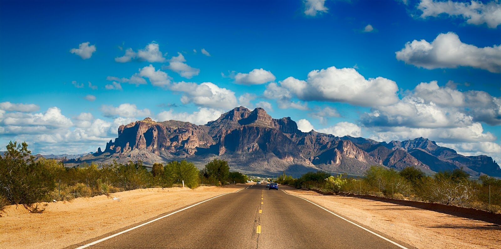 A long, empty Arizona highway leading toward desert mountains, the kind of drive that links Phoenix, Sedona and the Grand Canyon
