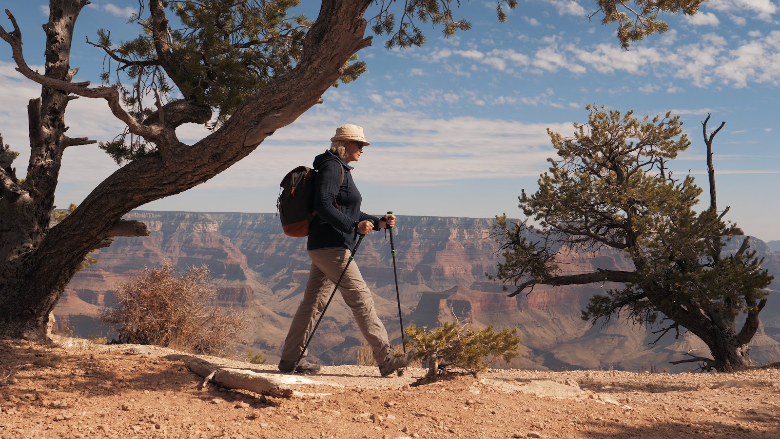 A hiker with trekking poles on a red rock trail on a clear morning, the reward for arriving at the trailhead early