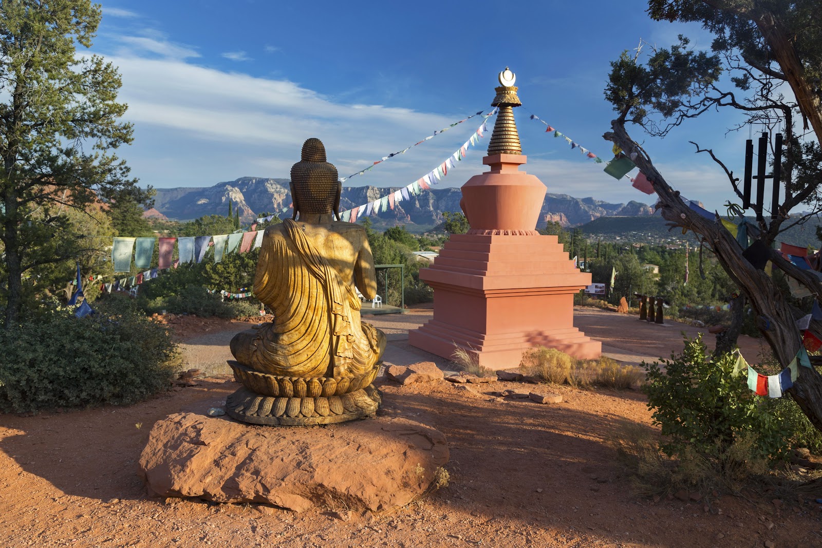 A Buddha statue and prayer flags facing Sedona's red rocks, a peaceful spot near the vortex sites